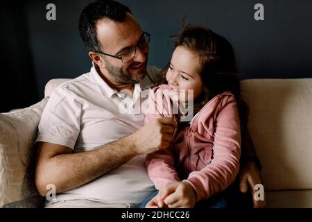 Smiling father looking at daughter while sitting on couch in living room Stock Photo
