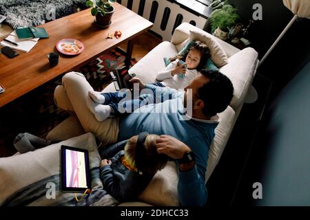 High angle view of father and daughters using various technologies on couch in living room at home Stock Photo