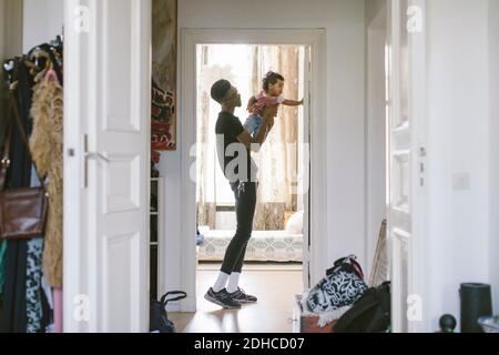 Side view of young man lifting daughter while standing at doorway in house Stock Photo