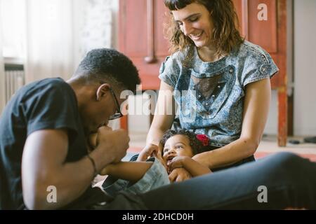 Father kissing foot of daughter lying on mother's lap at home Stock Photo