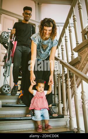 Mother holding hands of daughter moving down on steps in apartment Stock Photo