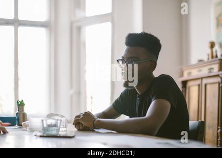 Thoughtful young man sitting at table in house Stock Photo