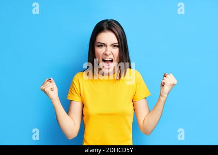 Screaming emotional angry young woman on blue background Stock Photo