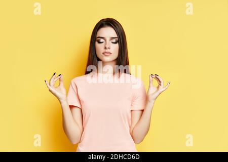 Relaxed pretty woman keeps hands in mudra gesture with eyes closed Stock Photo