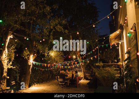 Multi-ethnic friends enjoying dinner party in illuminated backyard Stock Photo