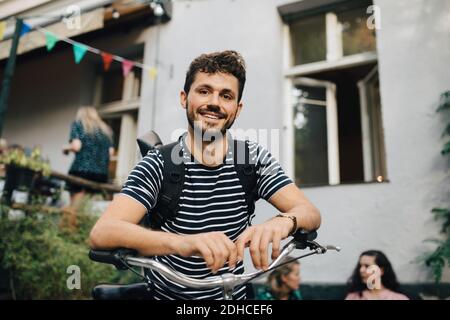 Portrait of smiling young man leaning on bicycle in backyard Stock Photo