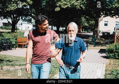 Smiling male caretaker looking while walking arm in arm with senior man at nursing home Stock Photo