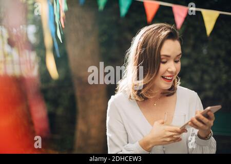 Smiling young woman using mobile phone while standing in backyard Stock Photo
