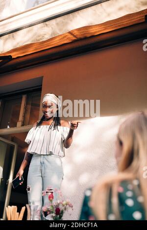 Smiling young woman pointing while standing in balcony Stock Photo