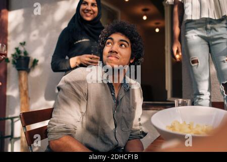 Young man looking up while sitting at table in balcony Stock Photo