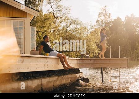 Mature man looking at woman using digital tablet while sitting on patio by lake Stock Photo