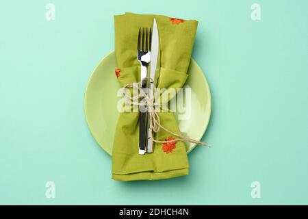 Empty round green ceramic plate and metal fork and knife, green background Stock Photo