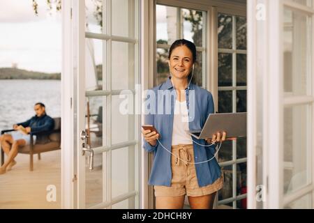 Portrait of mature woman using mobile phone and laptop with man in background Stock Photo