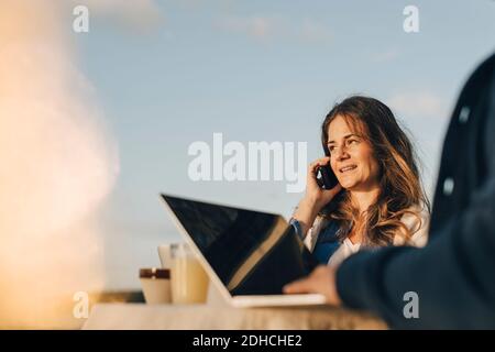 Thoughtful woman using mobile phone while sitting with man against sky Stock Photo