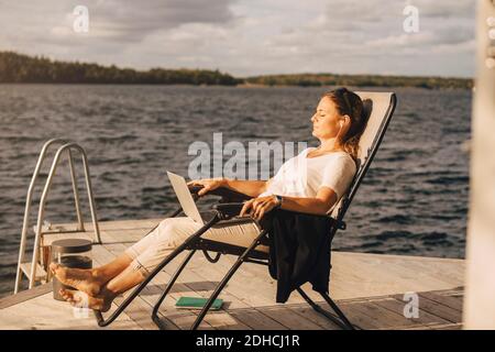 Full length of woman relaxing on deck chair at jetty over lake Stock Photo