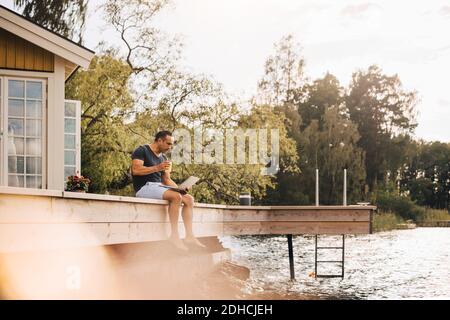 Mature man having juice while using laptop on patio by lake Stock Photo