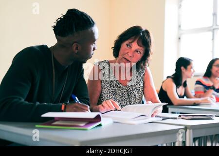 Senior teacher assisting student while sitting at desk in classroom Stock Photo