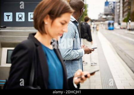 Commuters using smart phone while waiting on sidewalk in city Stock Photo