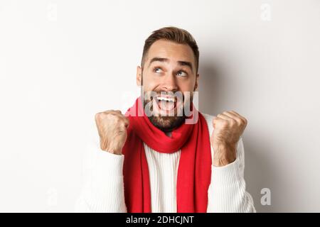 Christmas holidays. Close up of handsome man feeling excited about New Year party, fist pump and looking up amazed, white backgr Stock Photo