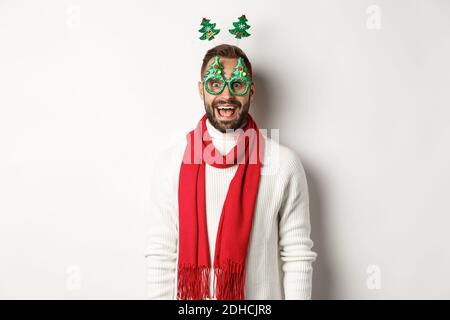 Christmas, New Year and celebration concept. Handsome bearded man looking surprised, wearing party glasses and accessory, white Stock Photo