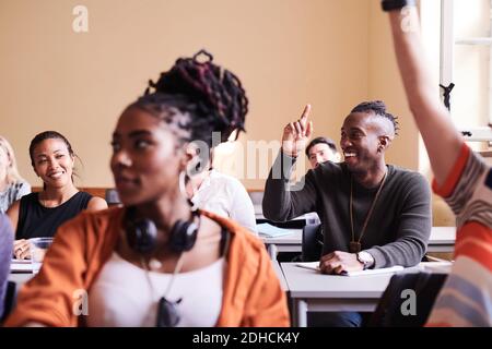 Happy young male student raising hand while sitting with classmates in school building Stock Photo
