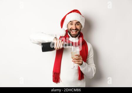Christmas party and holidays concept. Happy bearded man in Santa hat and scard, pour himself champagne and smiling, celebrating Stock Photo