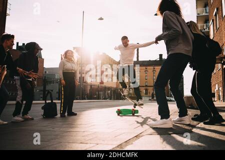 Male and female friends looking at young man doing stunt on skateboard at city Stock Photo