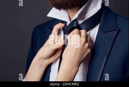 Womens hands tie around the neck of men classic suit model beard Stock Photo