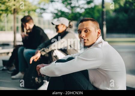 Portrait of young man sitting with friends at park Stock Photo