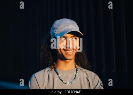 Close-up of smiling young man wearing cap looking away in dark Stock Photo