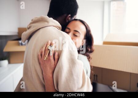 Close up of young mixed ethnicity couple holding keys to new home standing in kitchen hugging as they unpack removal boxes together Stock Photo