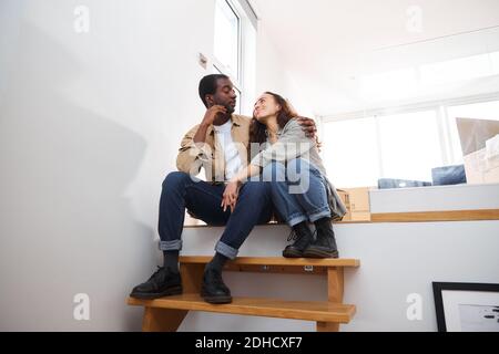 Young mixed ethnicity couple celebrating moving day in lounge of new home sitting on stairs surrounded by removal boxes together Stock Photo