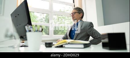 Businessman Having Back Pain While Sitting At Office Desk Stock Photo