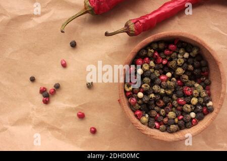 Various species multicolored peppers in wooden bowl, and dry red hot chili peppers on craft paper background. Top view, copy space Stock Photo