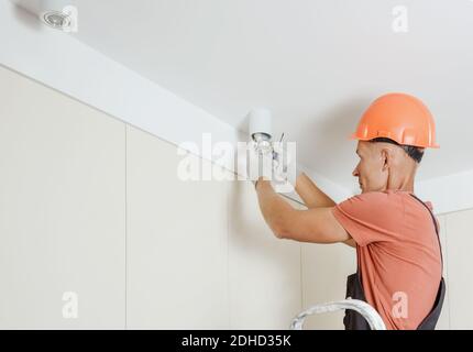 A worker is installing an LED spotlight on the suspended ceiling. Stock Photo