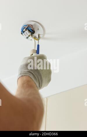 A worker is installing an LED spotlight on the suspended ceiling. Stock Photo