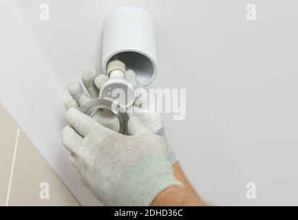A worker is installing an LED spotlight on the suspended ceiling. Stock Photo