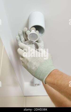 The worker is installing an LED spotlight on the suspended ceiling. Stock Photo