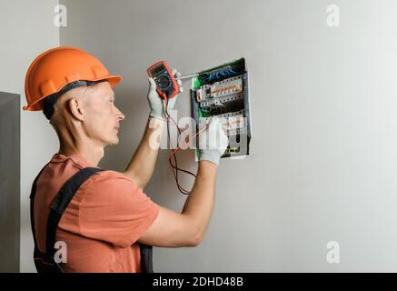The electrician is checking with a multimeter the correctness of the connection of the circuit breaker. Stock Photo