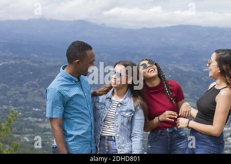 group of four Latin American adventurers friends three women one man outdoors laughing and joking using sunglasses nature in background in a summer da Stock Photo