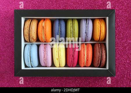 Multicolored macarons in a cardboard box without a lid on a magenta glitter surface. View from above. Closeup Stock Photo