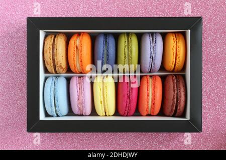 Multicolored macarons in a cardboard box without a lid on a pink glitter surface. View from above. Closeup Stock Photo