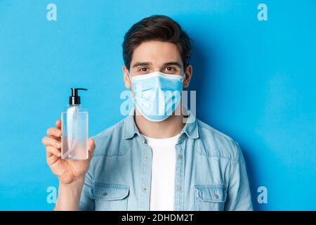 Concept of coronavirus, pandemic and preventive measures. Close-up of young man in medical mask advice to use hand sanitizer, sh Stock Photo