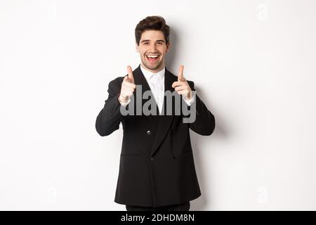 Concept of new year party, celebration and lifestyle. Handsome and successful guy in black suit, pointing fingers at camera and Stock Photo