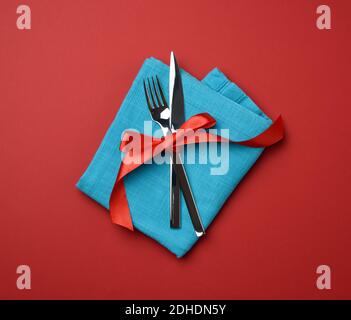 Metal fork and knife tied with a red silk ribbon, red background Stock Photo