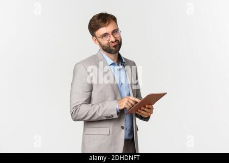 Portrait of businessman with beard, wearing glasses and grey suit, disappointed with bad work, holding digital tablet and grimac Stock Photo
