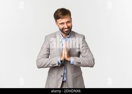 Portrait of happy bearded businessman in grey suit, thanking for something, holding hands pressed together and bowing with grate Stock Photo
