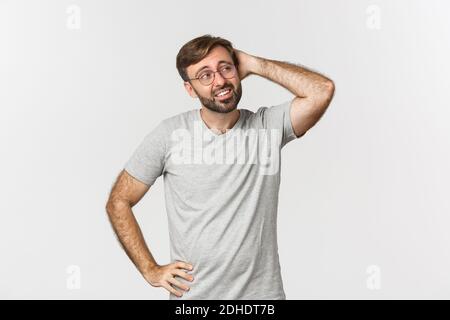 Portrait of indecisive adult man thinking, scratching head and looking confused at upper right corner, standing in gray t-shirt Stock Photo
