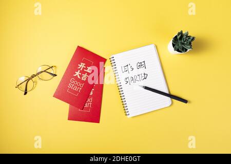 A notebook with "LET'S GET STARTED" text and good start red envelopes on yellow background Stock Photo