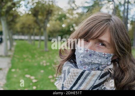 Portait of woman wearing a white coat and a medical mask observing a green field from a park. vacation concept Stock Photo